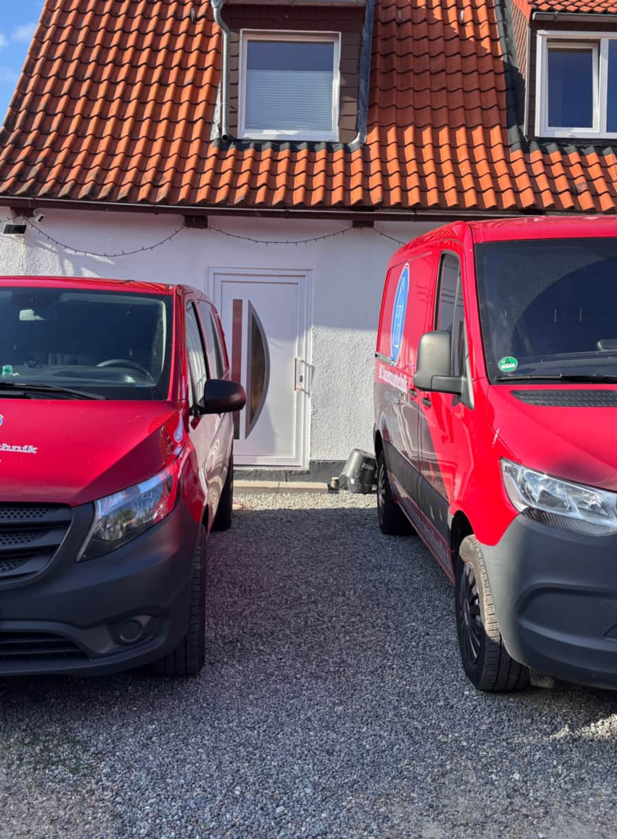 Zwei rote Einsatzfahrzeuge von MS Sanierungstechnik vor einem Wohnhaus